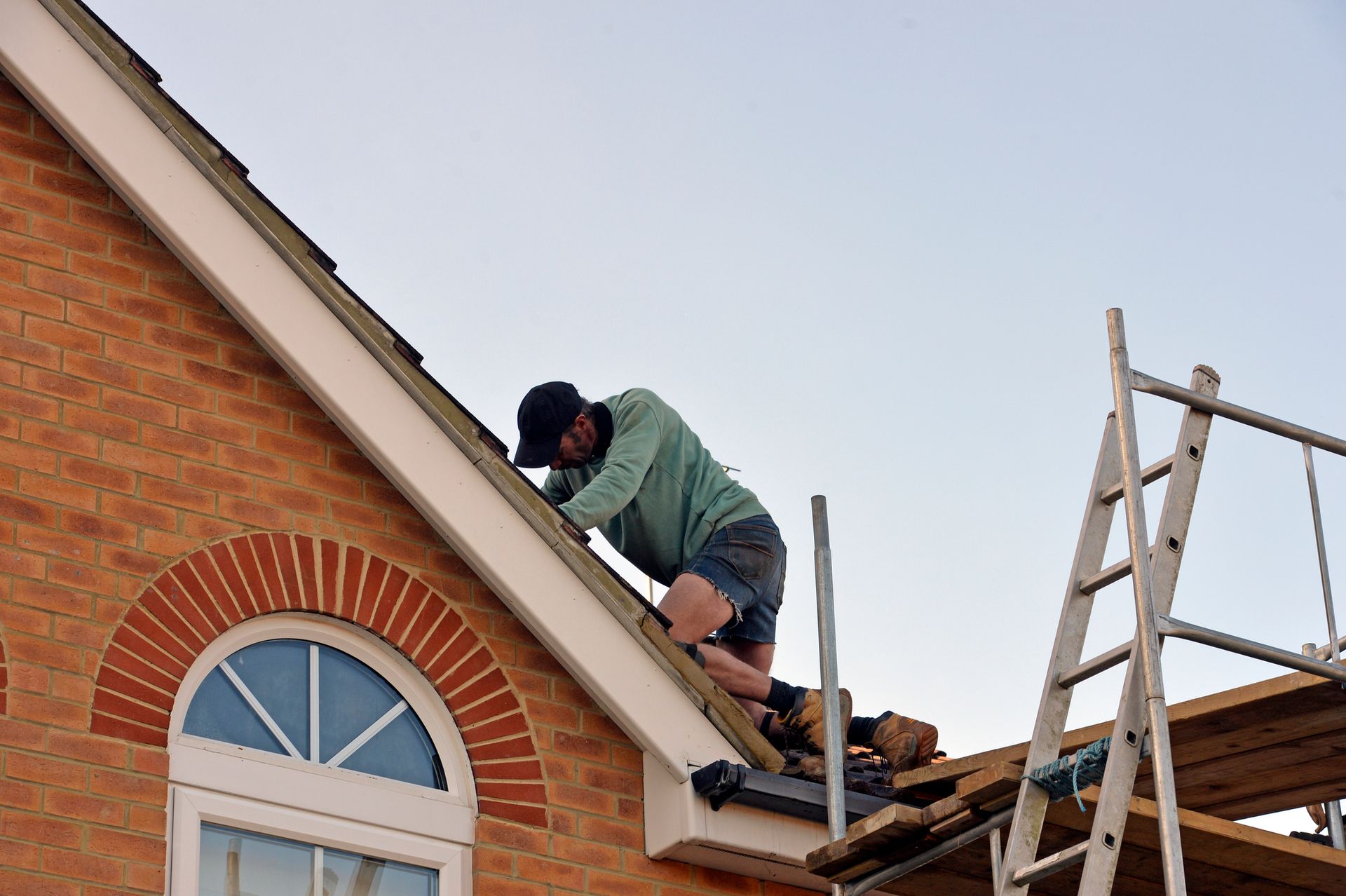 Person working on a house roof near a ladder during construction. Person working on a house roof near a ladder during construction.