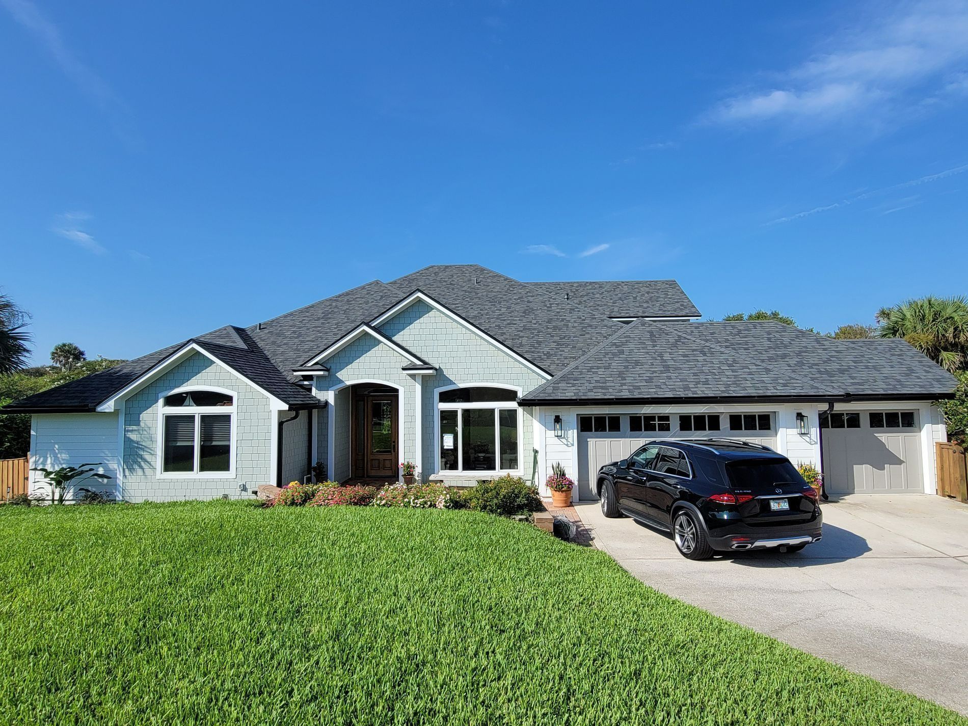 This image features a modern single-story house with light-colored siding and a dark shingled roof.
