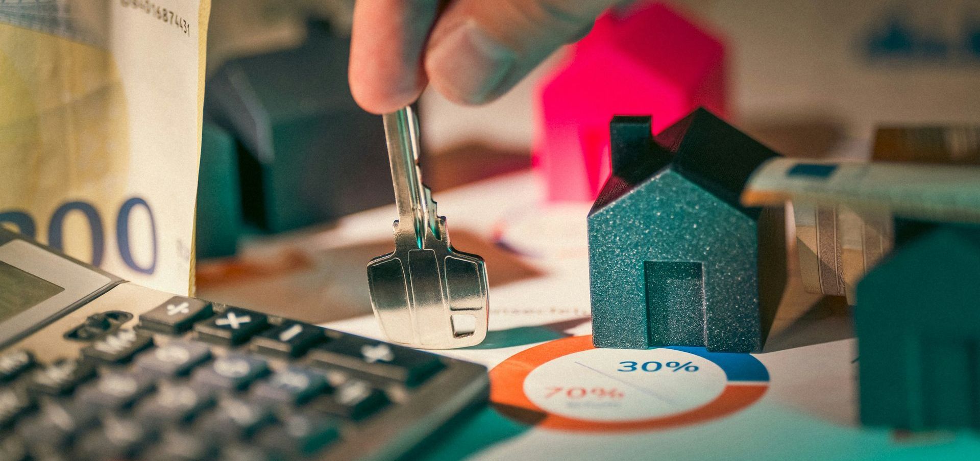 Hand holding key above a tiny house next to a calculator, money, and charts. Financial planning or real estate concept.