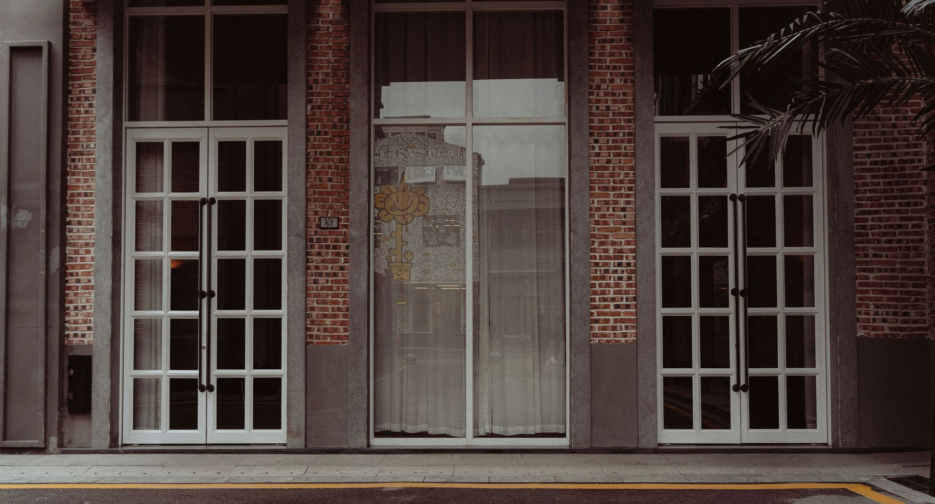 Exterior of a building with white paneled doors and windows, brick pillars, and a gray facade.