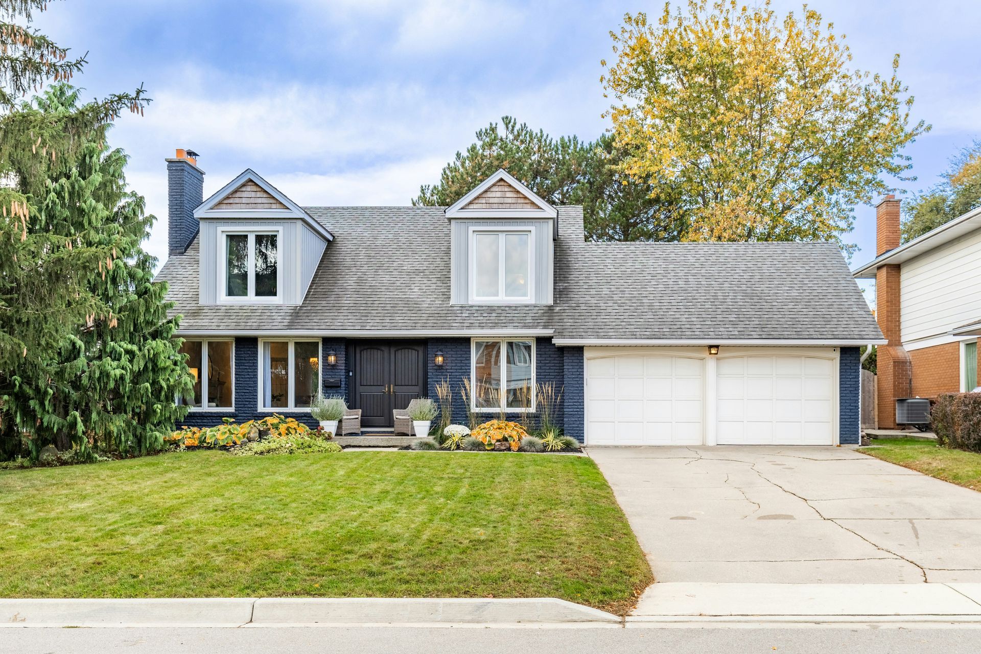 Front view of a two-story blue house with a gray roof and two-car garage; lush green lawn with fall foliage.