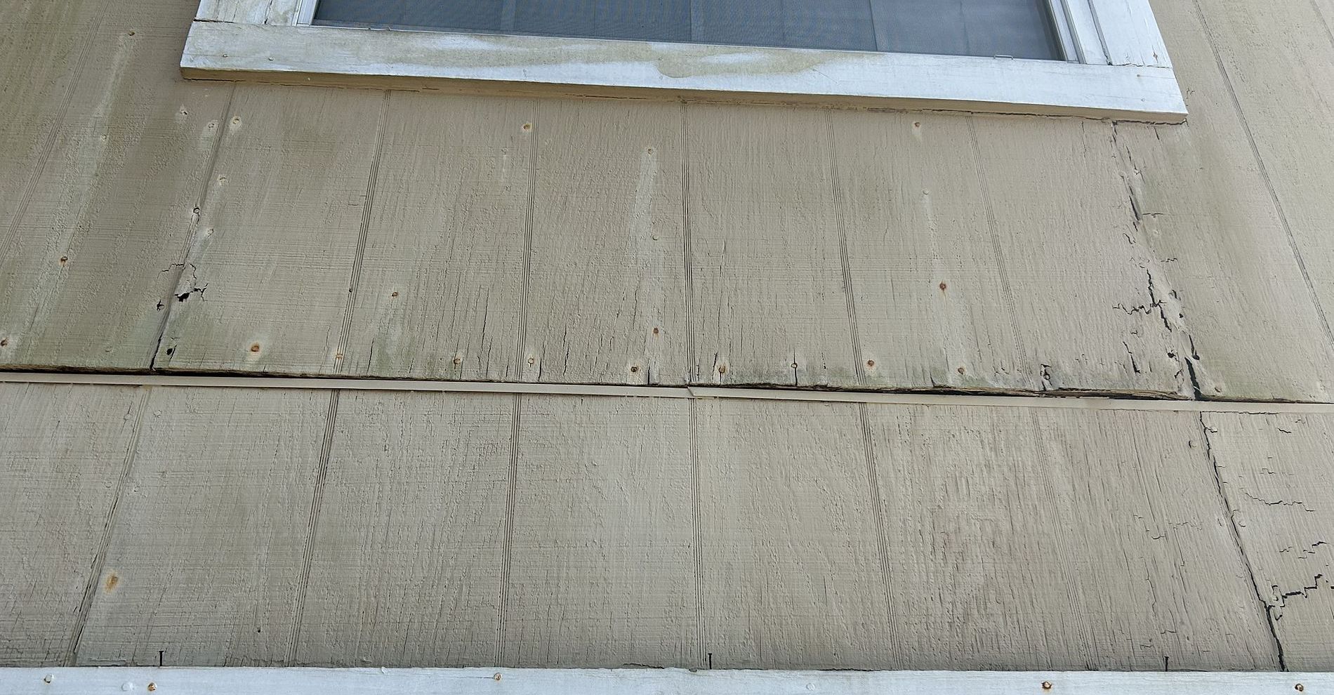 Beige stucco exterior wall with a window, showing cracks and discoloration.