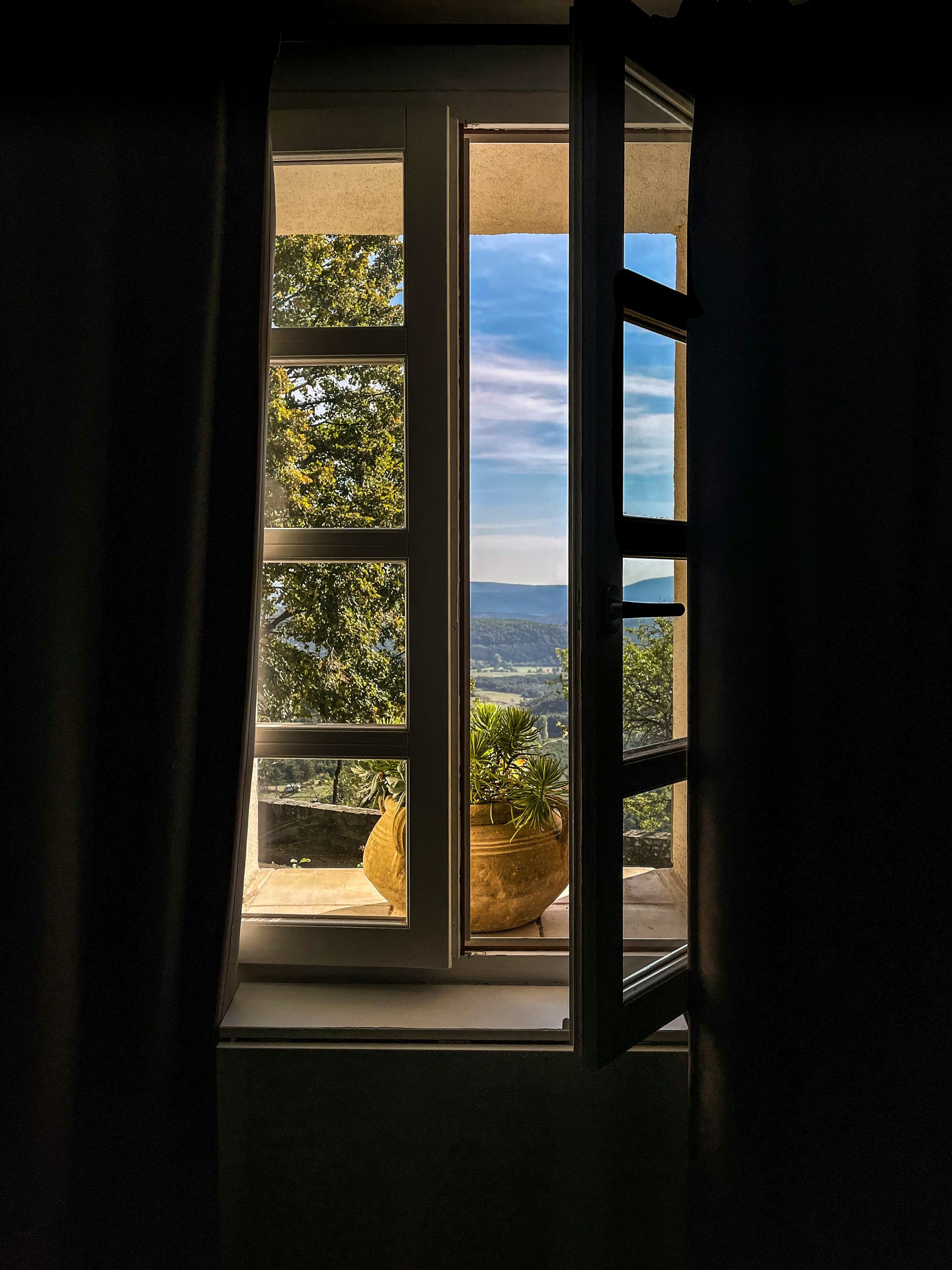 Open window with view of green trees, blue sky, and distant hills.