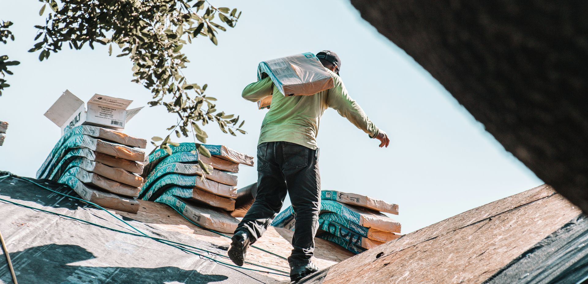 A construction worker carrying materials on a rooftop, with stacks of materials visible.