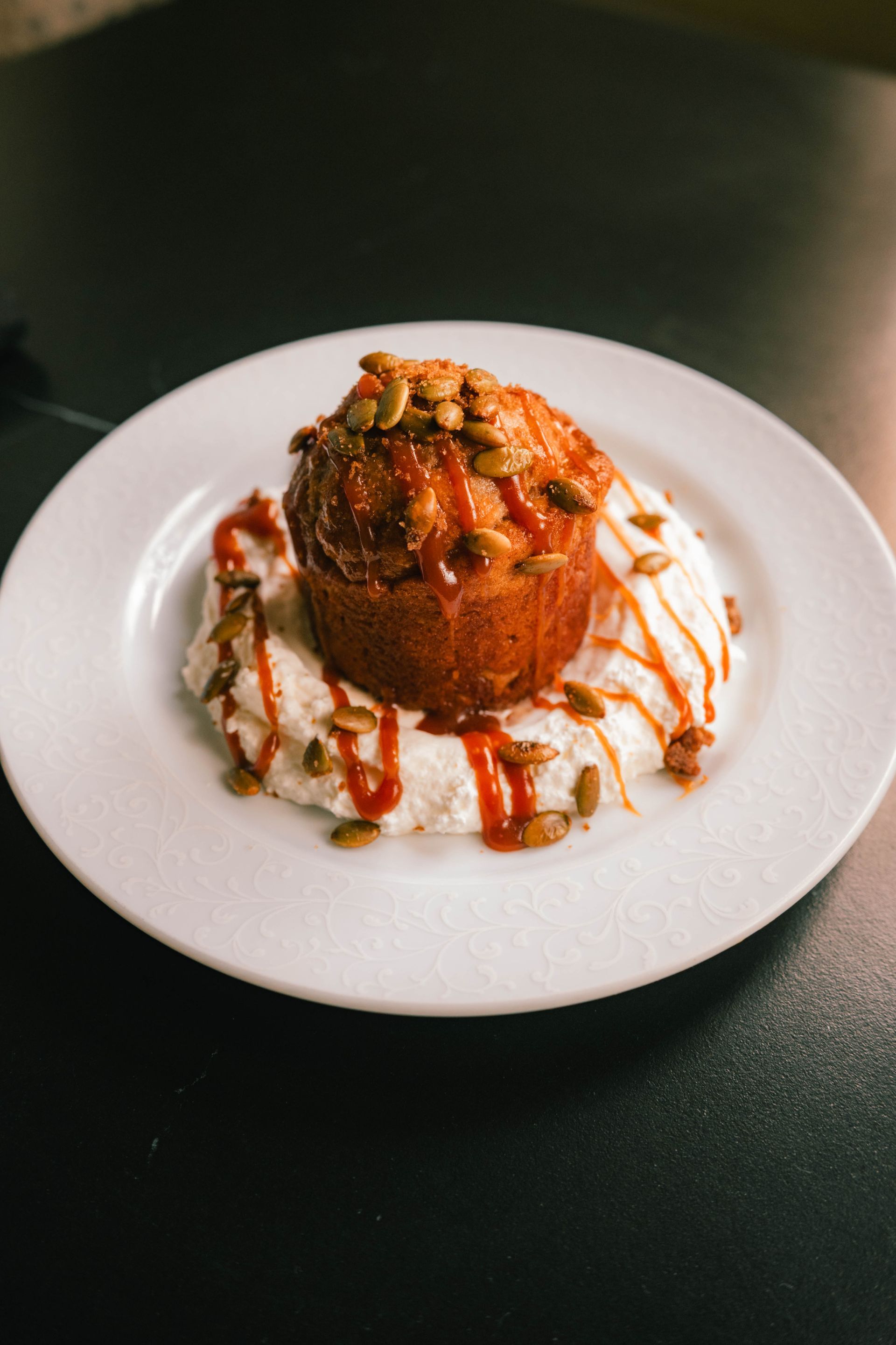 Dessert with caramel drizzle and nuts on a white plate against a dark table