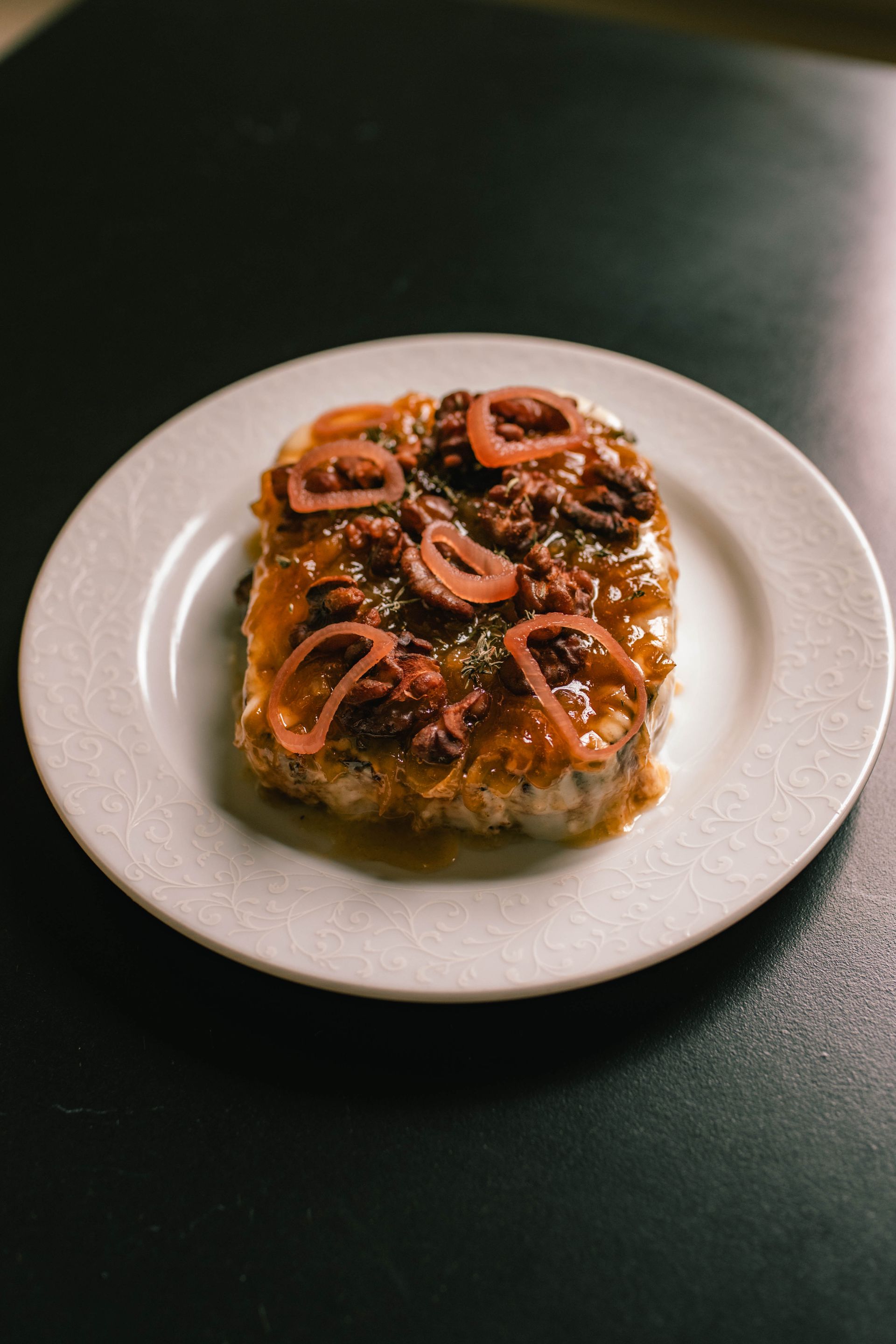 Glazed pastry topped with pretzel pieces on a white plate on a dark table