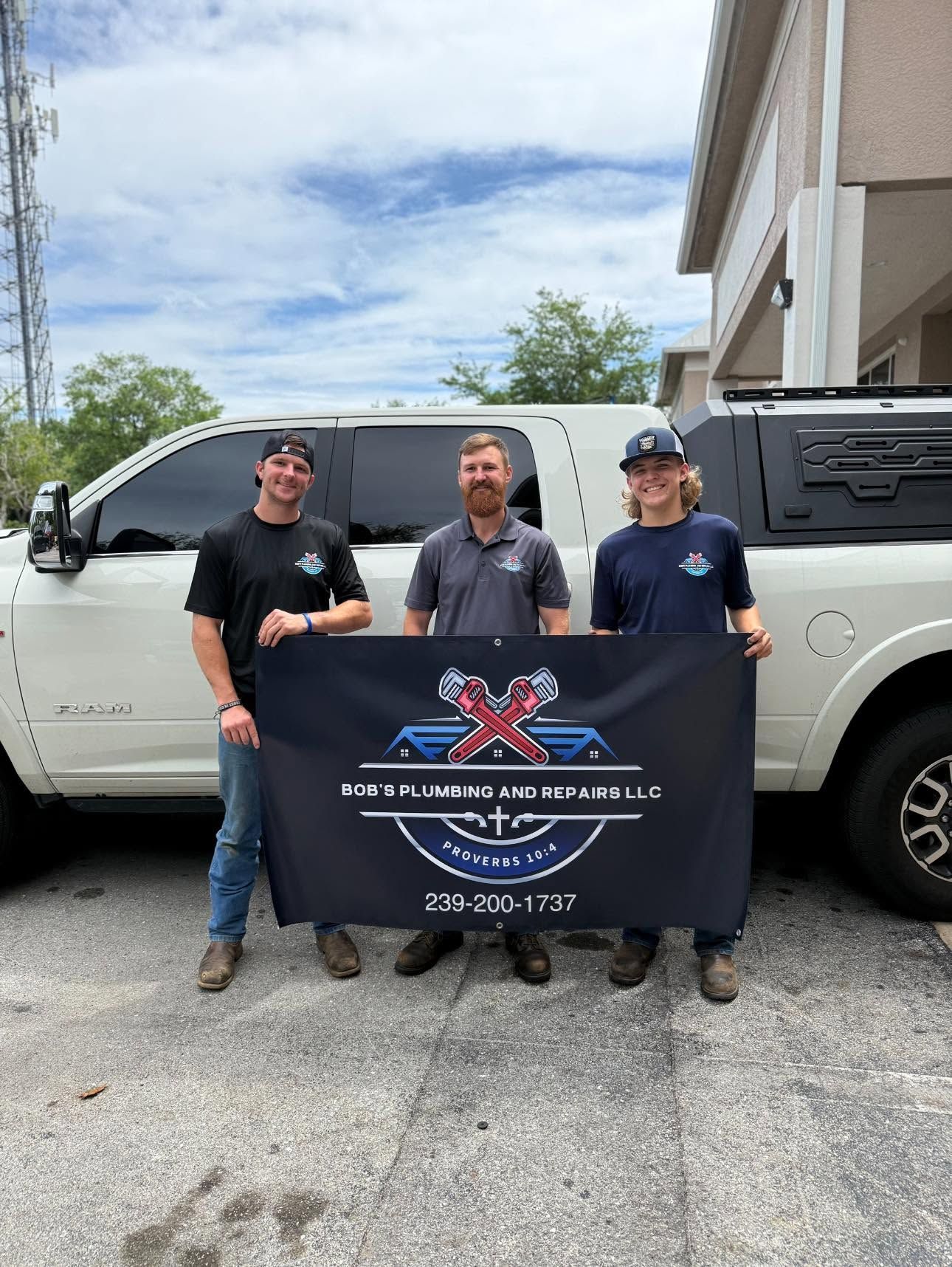 Three workers standing beside a white pickup truck, holding a company banner outdoors.