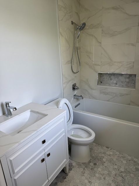 Modern bathroom with white vanity, toilet, bathtub, and marble-patterned walls and floor