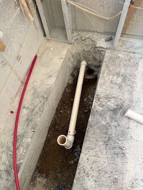 Open trench with a white PVC pipe running through a concrete basement floor.
