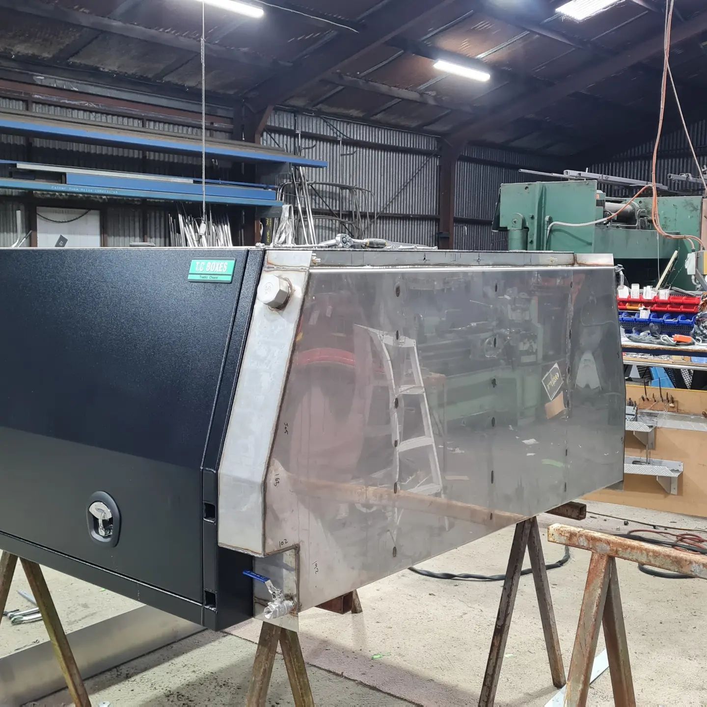 Large industrial metal machine in a workshop, with a clear front panel and dark side housing.