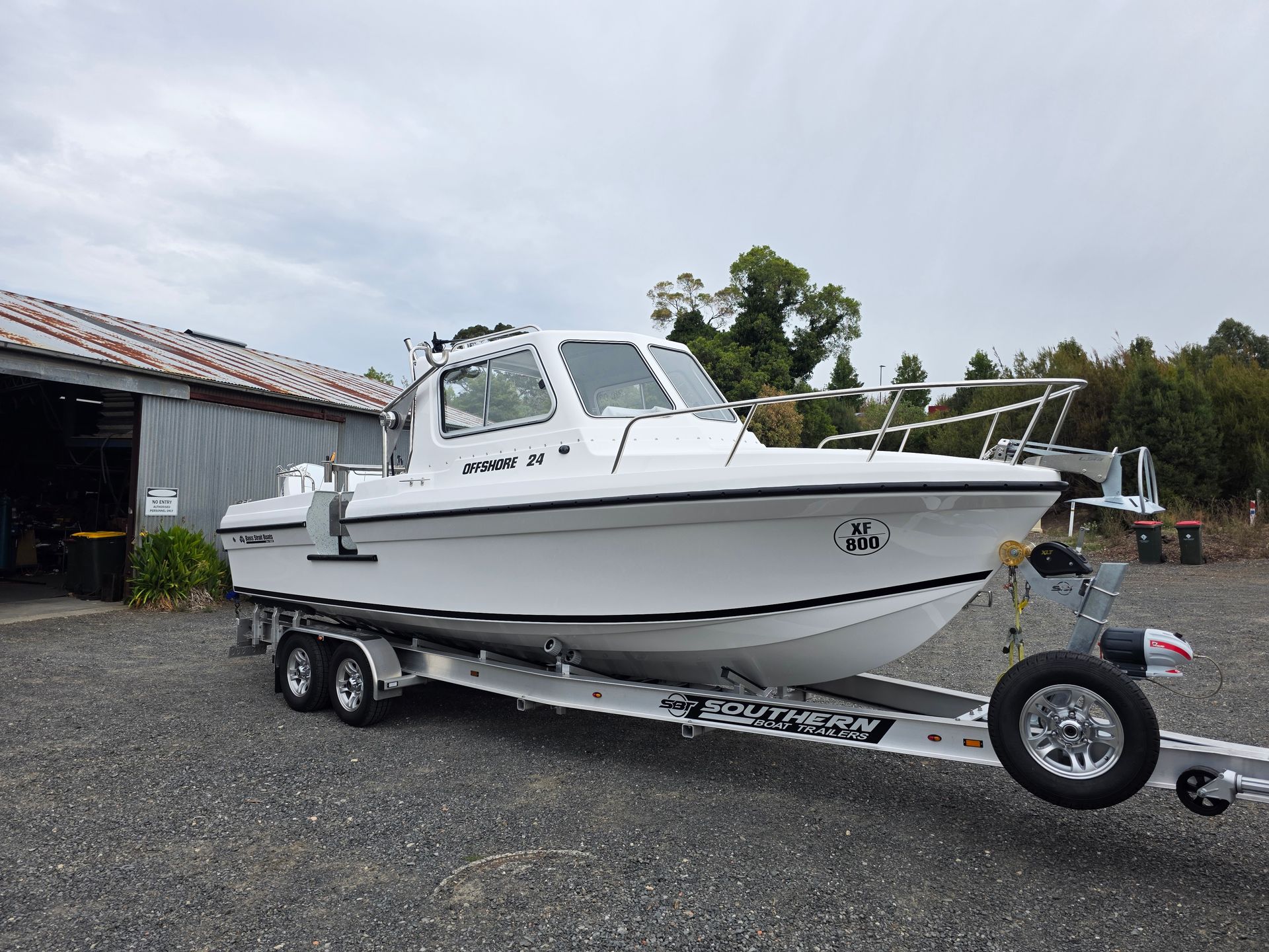 White fishing boat on a trailer in a gravel lot under an overcast sky