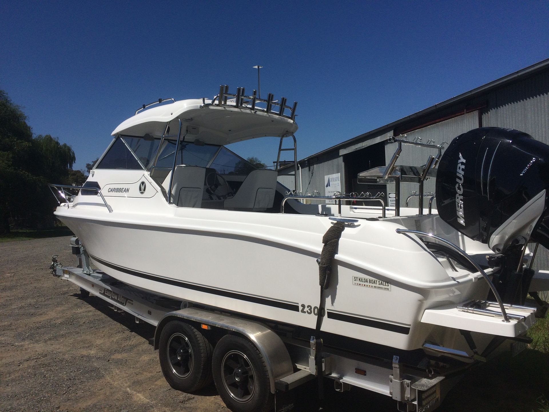 White speedboat on a trailer with a canopy, parked outdoors in bright sunlight.