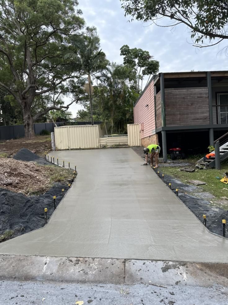 A Man Is Working On A Concrete Driveway In Front Of A House — Hinterland Concreting Pty Ltd In Lennox Head, NSW