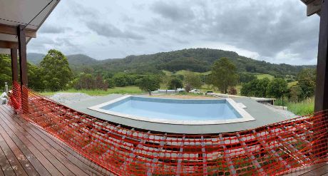A Large Swimming Pool Is Surrounded By A Fence And Mountains In The Background — Hinterland Concreting Pty Ltd In Casino, NSW