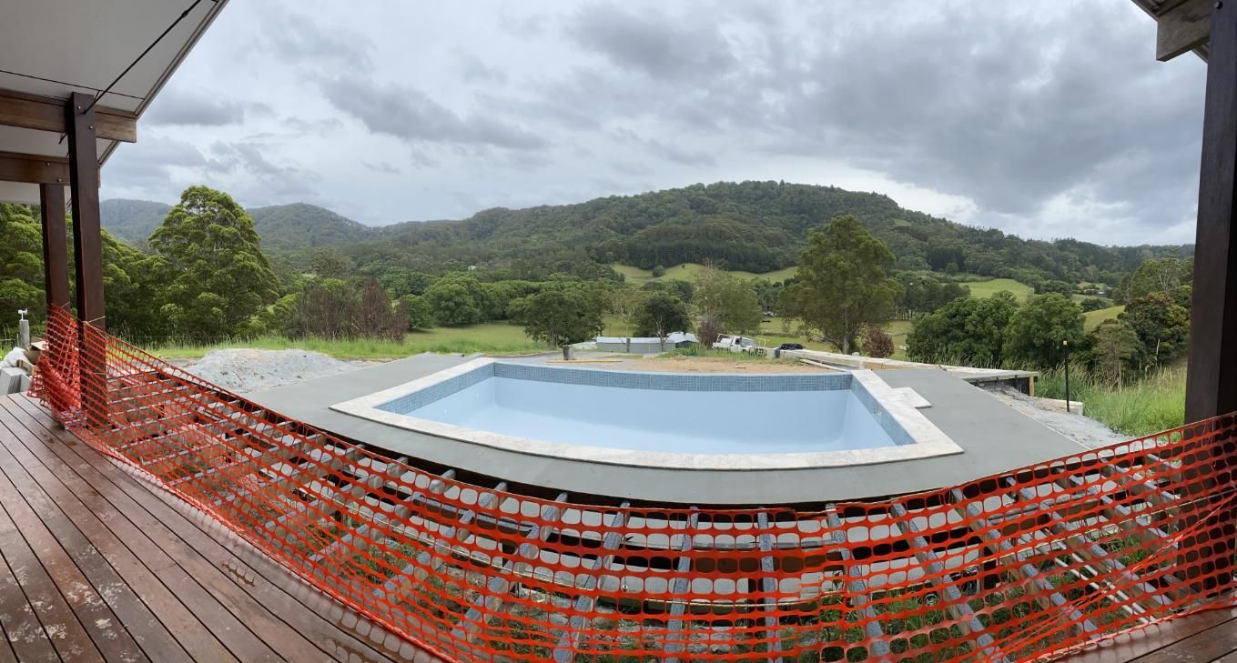A Large Swimming Pool Is Surrounded By A Fence — Hinterland Concreting Pty Ltd In Lennox Head, NSW