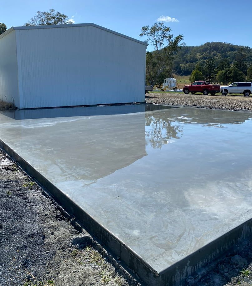 A White shed With A Red Truck Parked In Front Of It — Hinterland Concreting Pty Ltd In Lennox Head, NSW