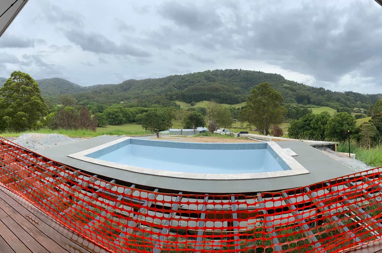 A Large Swimming Pool Is Surrounded By A Fence And Mountains — Hinterland Concreting Pty Ltd In Lennox Head, NSW