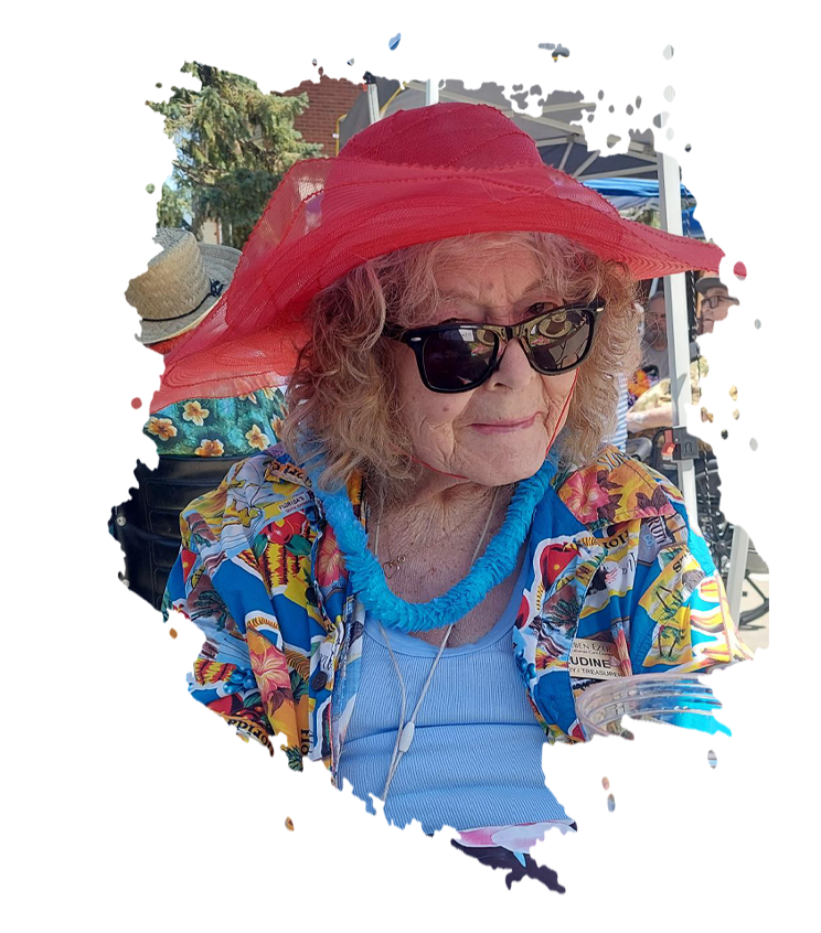 Person in floral shirt, heart-shaped sunglasses, and lei smiles at an outdoor event with tents.