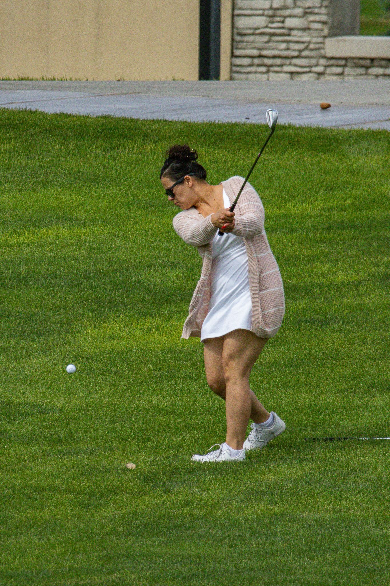 Golfer in white dress swinging a club on a grassy course