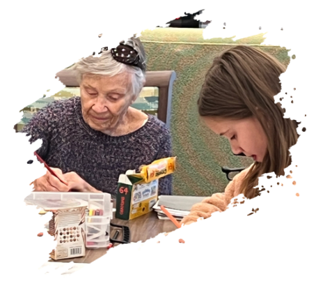 An elderly woman and young girl sit at a table, drawing. They are focused and sharing supplies.