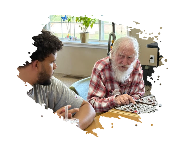 Man in wheelchair talking to a woman, indoors. Man has a beard, hat. Woman smiles, listens.