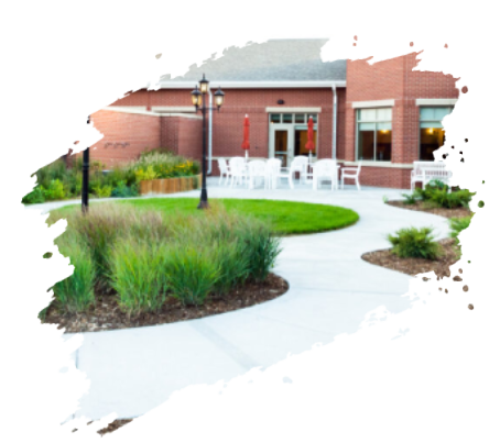 Brick building patio with white chairs, small lawn, and landscaping.
