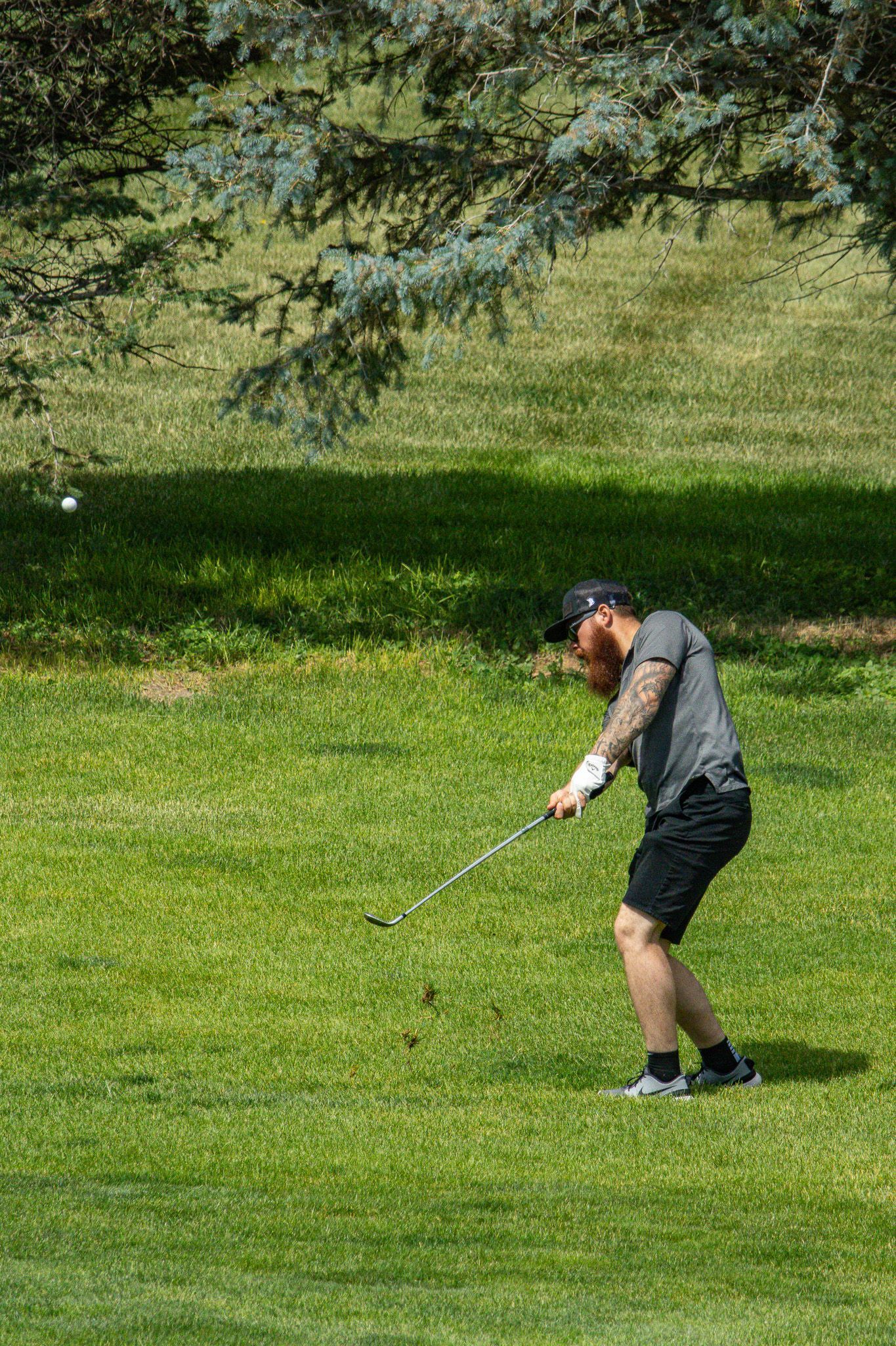 Golfer in black outfit swinging a club on a green fairway under trees