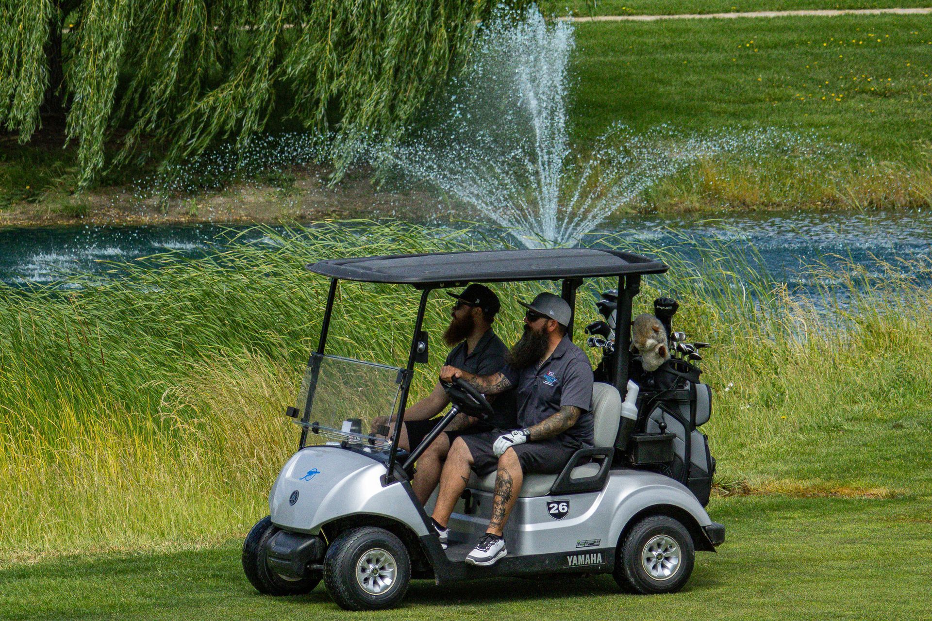 Golf cart driving through a grassy course with water spraying in the background