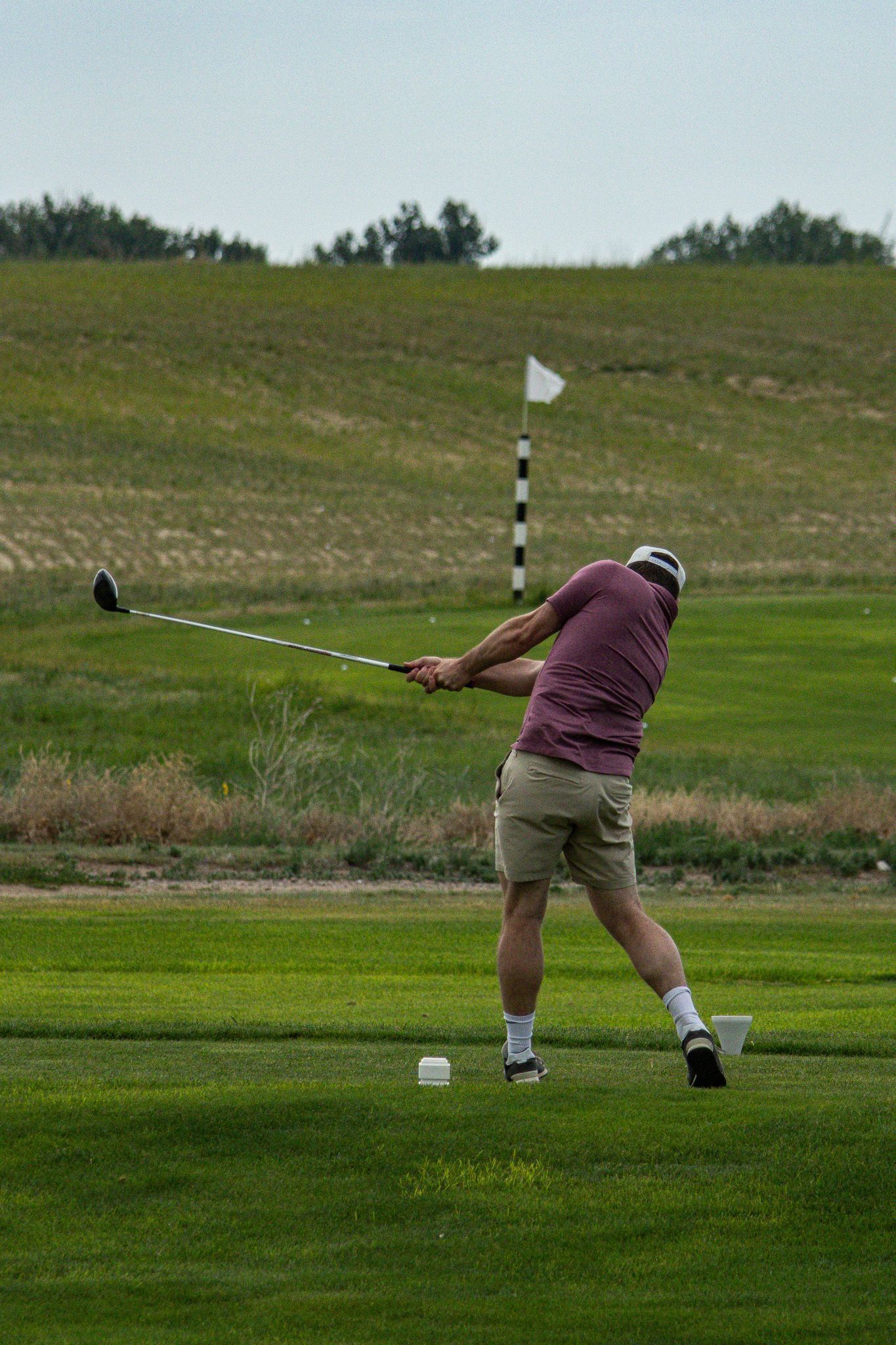 Golfer in maroon shirt swinging club on a grassy course near a flagstick