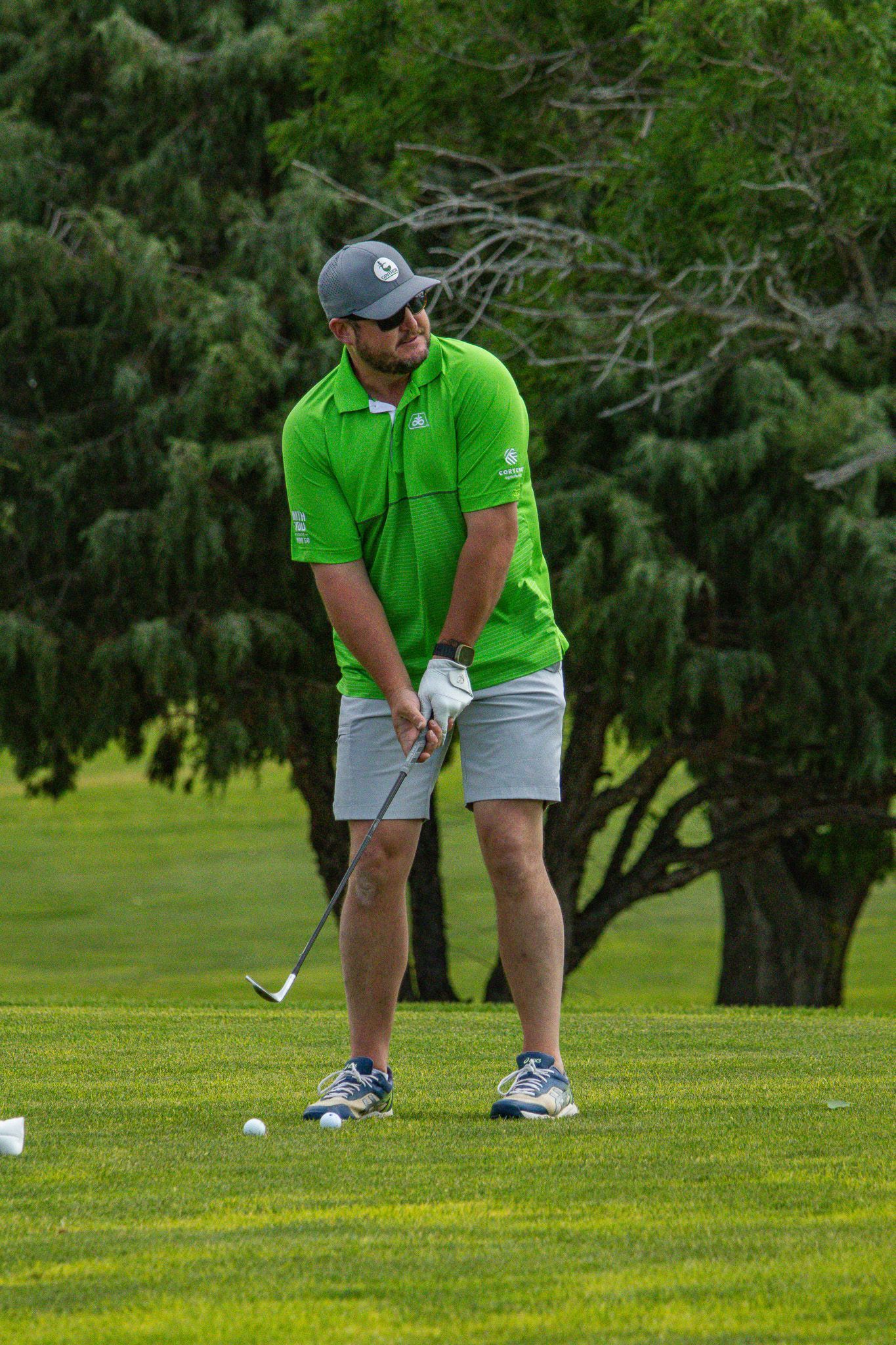 Golfer in a bright green shirt preparing to hit a ball on a grassy course