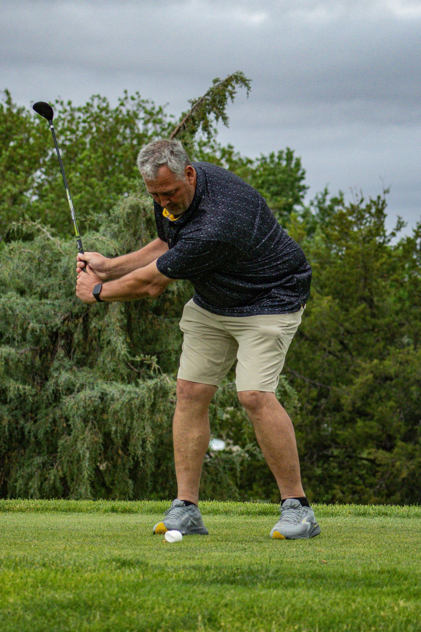 Golfer mid-swing on a green course under cloudy skies