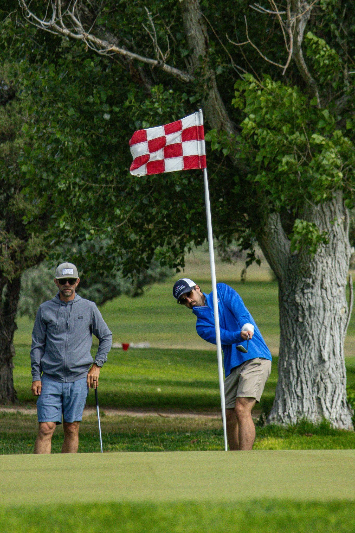 Golfer putting on a green beside a red-and-white checkered flag at the hole