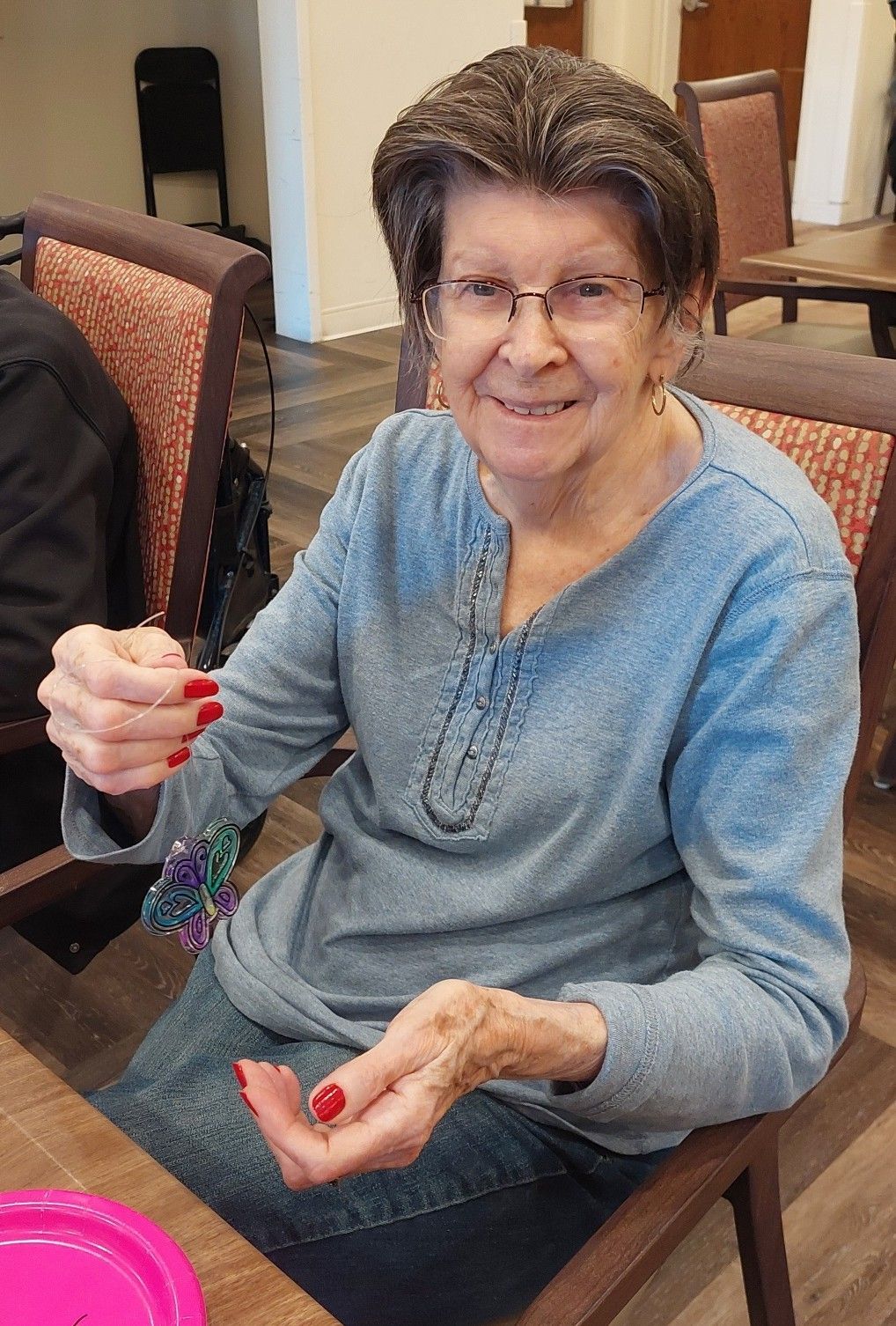 A person with short brown hair and glasses wears a blue shirt while holding a small, colorful beaded ornament.