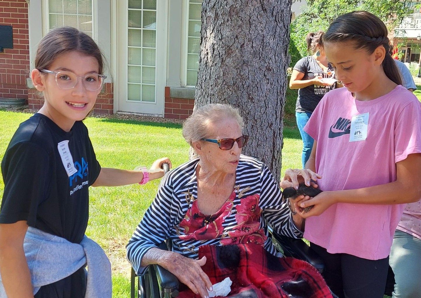 Two children standing outdoors next to a woman in a wheelchair, who is holding a small animal.