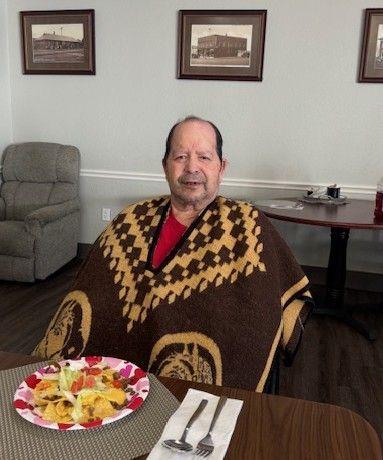A person wearing a brown and tan patterned poncho sits at a table with a plate of food and silverware.