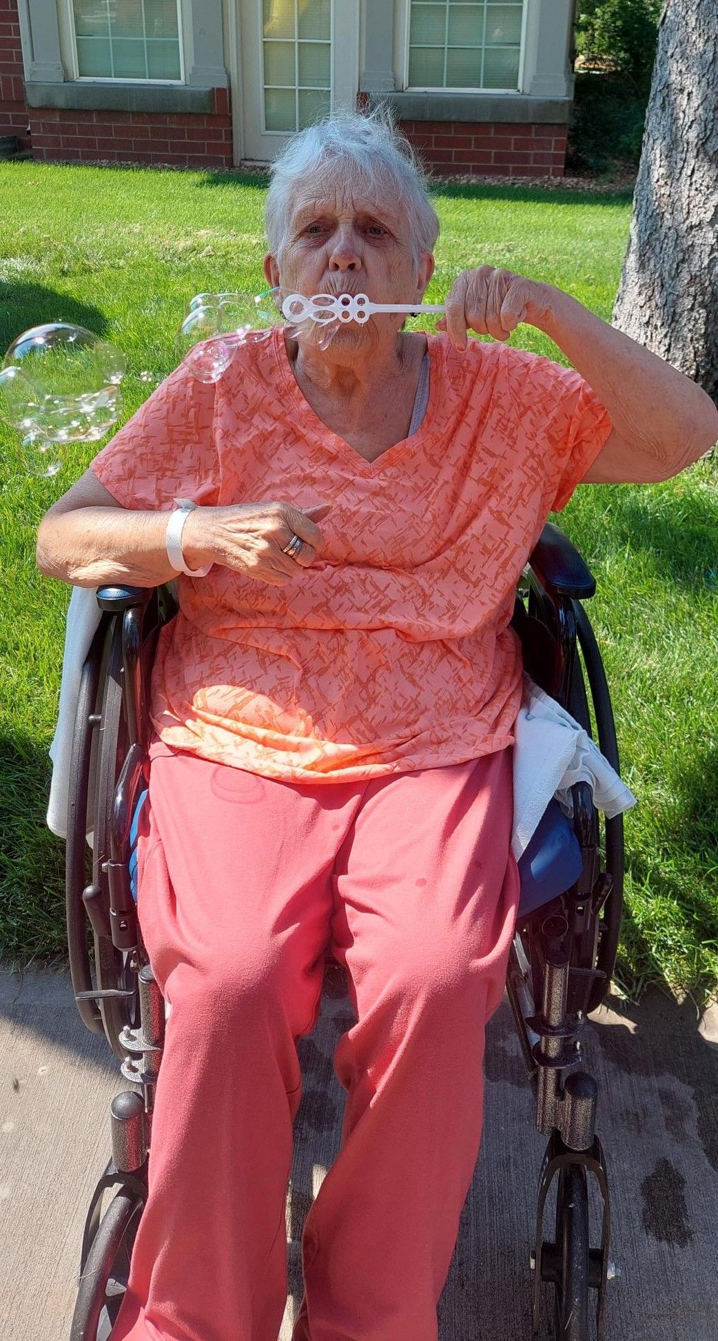 A person in a wheelchair blows bubbles outdoors in front of a brick building.