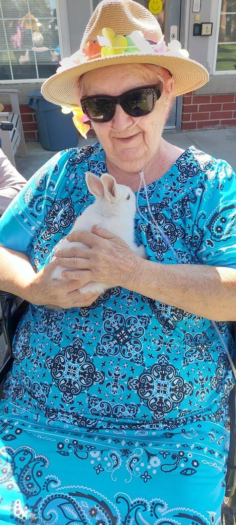 A person wearing a straw hat and sunglasses holds a small, white rabbit against their bright blue patterned top.