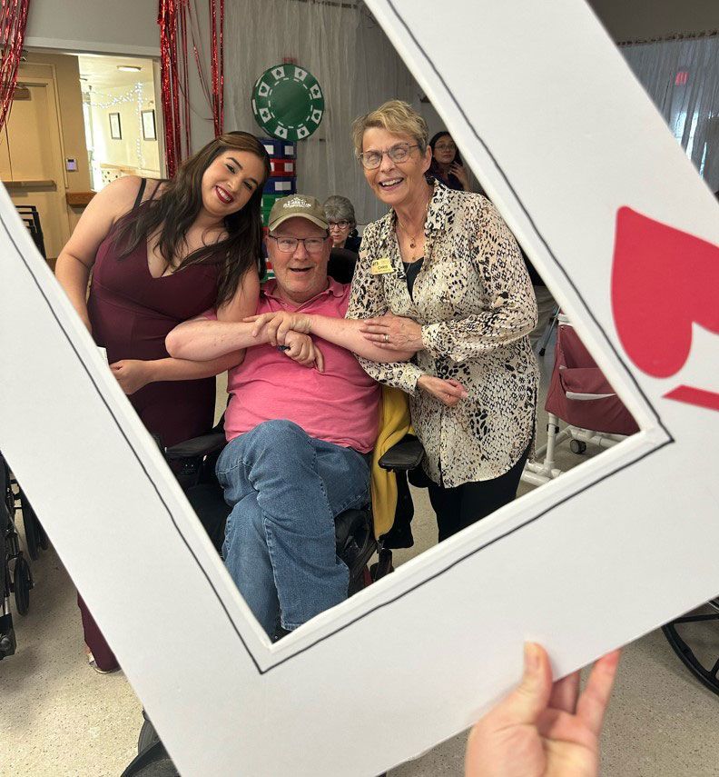 Three smiling people pose behind a heart-shaped photo frame at a festive event.