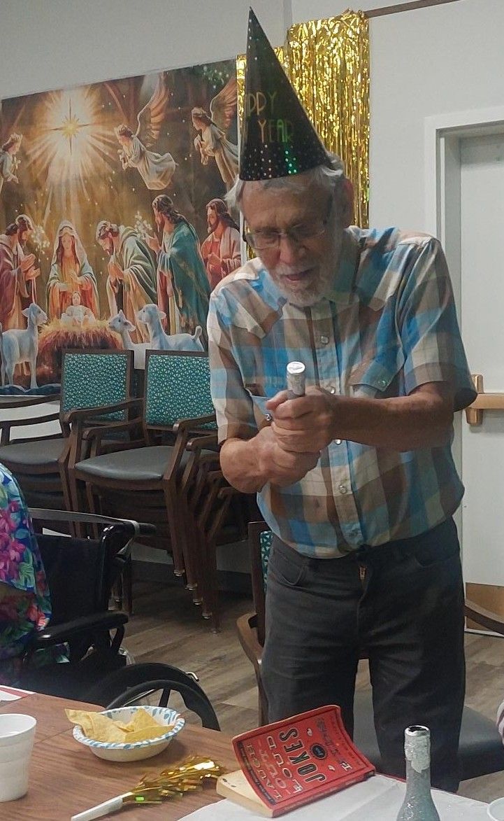 A person wearing a party hat holds a small party popper in an indoor setting with a religious mural in the background.
