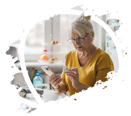 Older woman in glasses, holding phone and medication bottle in kitchen.