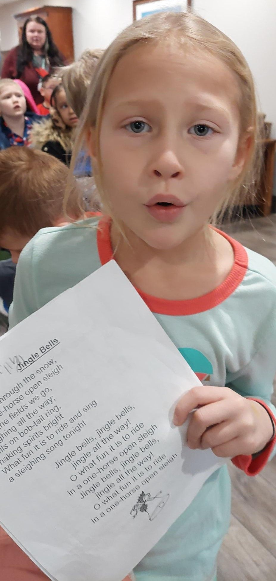 A child holds up a handwritten letter in a room with other people.