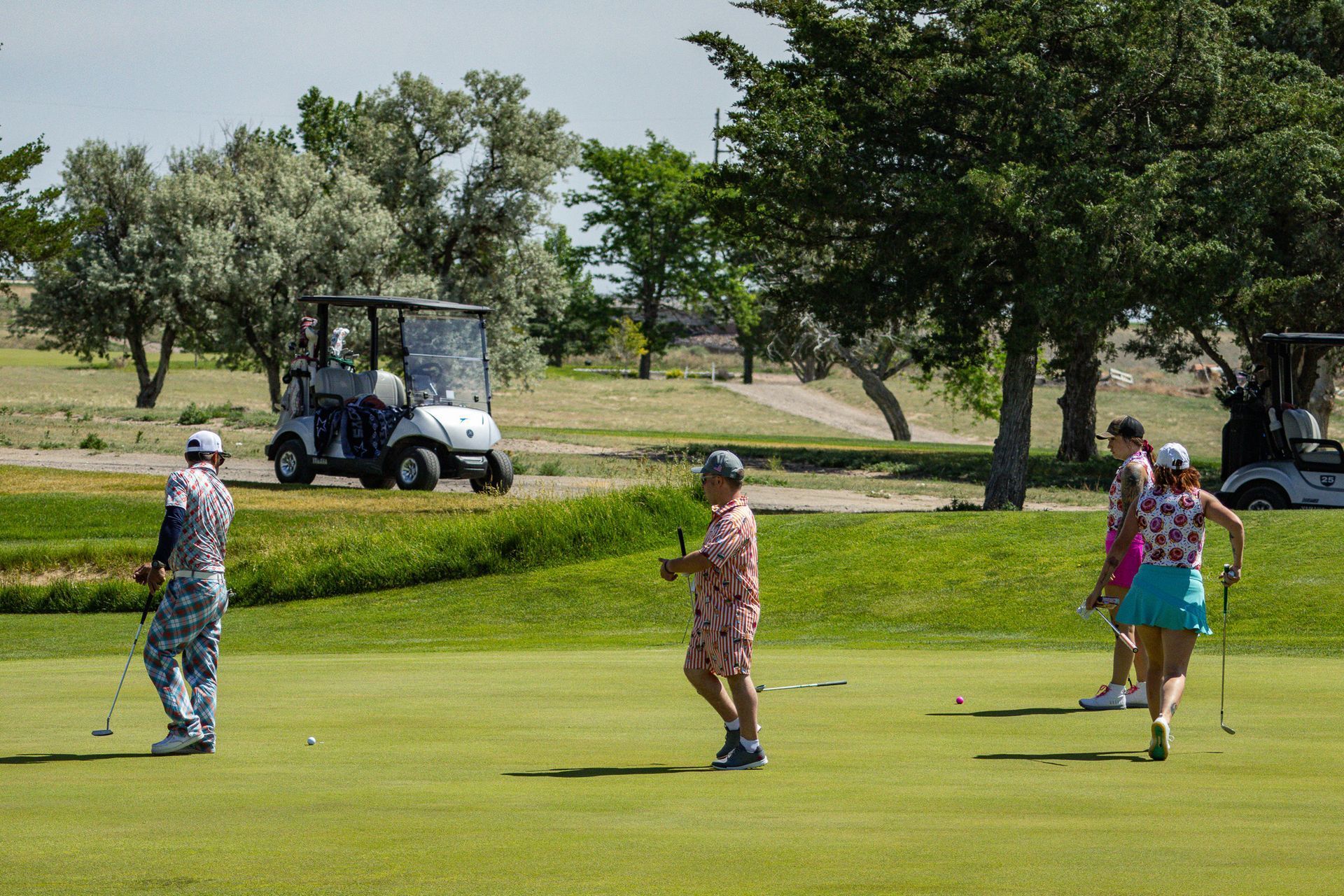 Golfers putting on a green with a golf cart and trees in the background