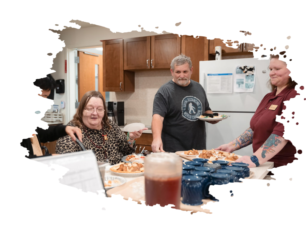 Three people in a kitchen setting serve food from plates onto a counter, including a drink in the foreground.