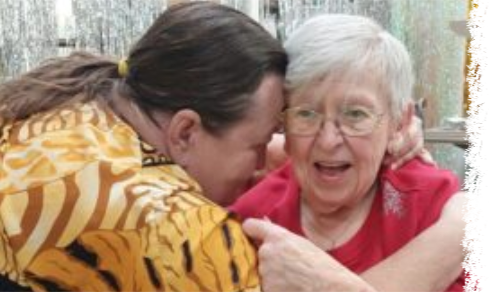 Two people embracing, leaning their foreheads against each other in an affectionate, indoor setting.