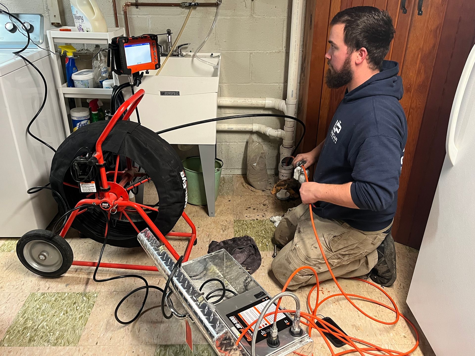 a man is kneeling down in a laundry room using a drain camera .