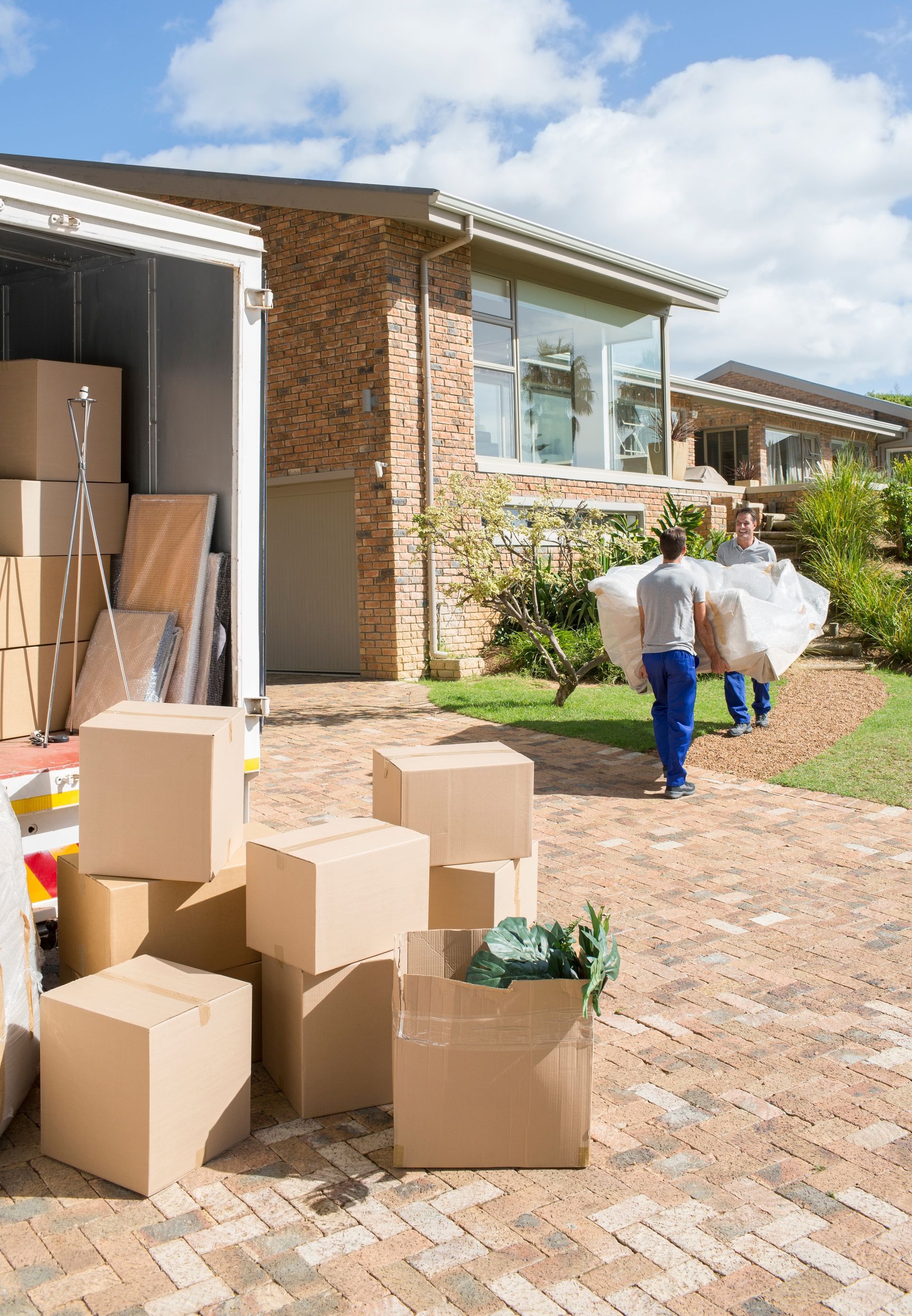 Moving boxes outside a house, with a person carrying a large white bundle toward the driveway.