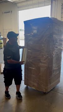 Worker standing beside a tall pallet wrapped in clear plastic in a warehouse loading area