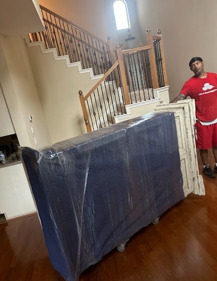 Wrapped furniture and a staircase leaning against a wall in a room; a man stands nearby.