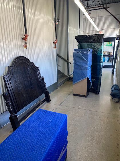 Storage area with a black headboard and blue-wrapped furniture stacked along a wall.