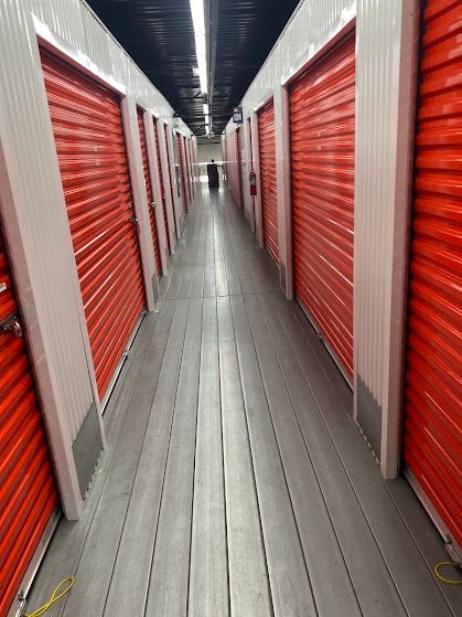 A narrow storage aisle with red roll-up doors and a gray floor under bright overhead lights.